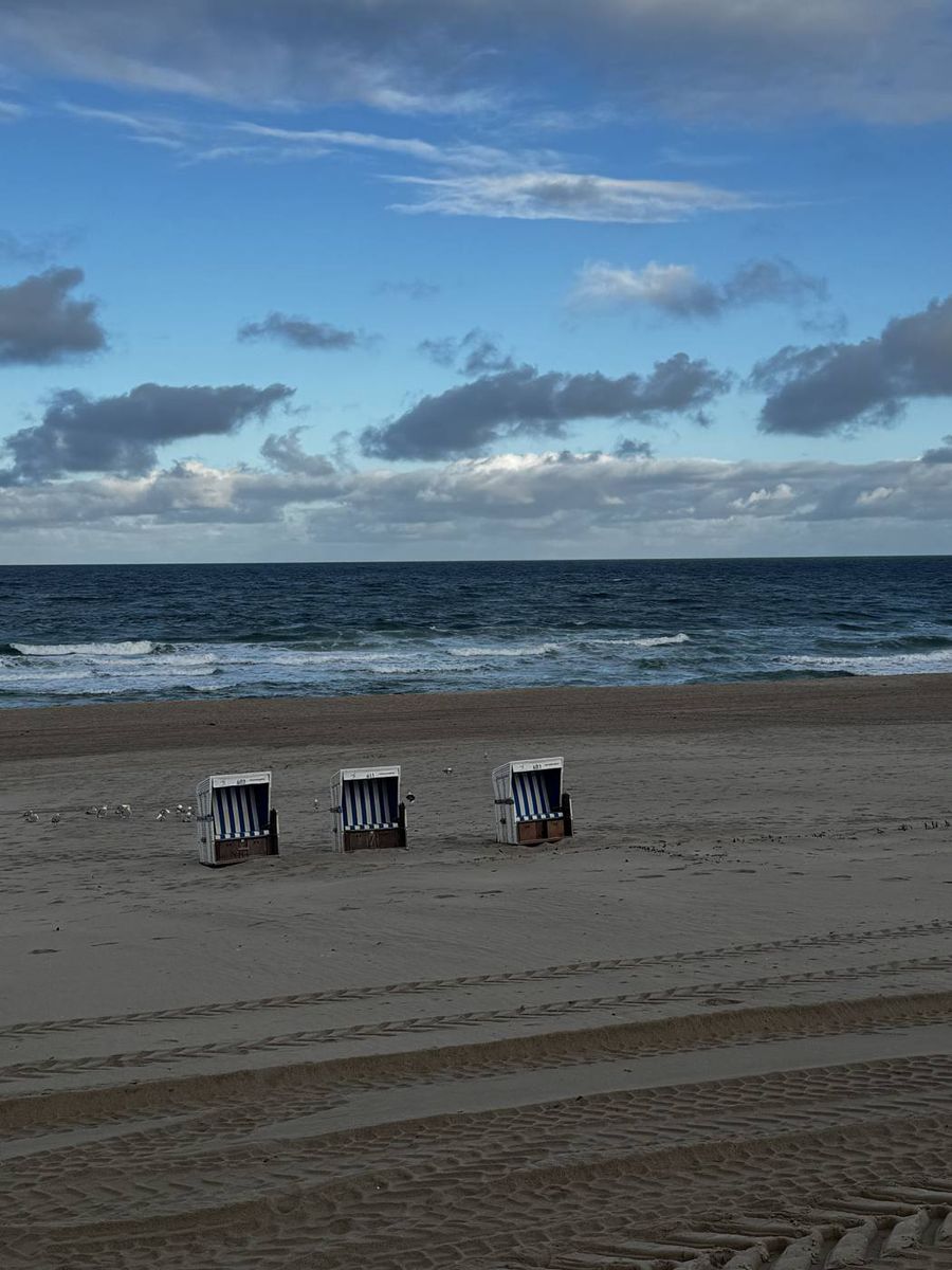 Drei einzelne Strandkörbe vor der bewegten Nordsee auf Sylt
